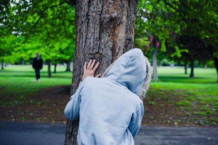 A suspicious character wearing a hoodie is hiding behind a tree in the parkの写真素材