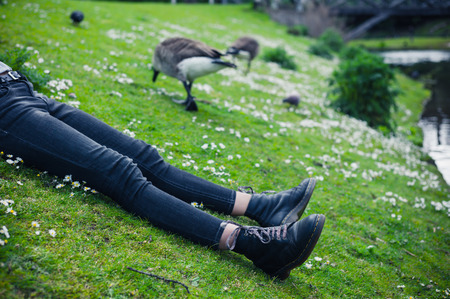 The legs of a young woman as she is lying on the grass by a pond in a parkの写真素材