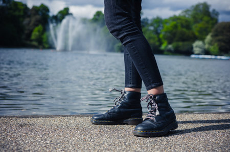 The legs of a young woman as she is standing by a a pond in the park