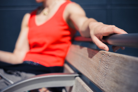 A young woman is resting on a bench outside on a sunny dayの写真素材