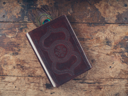 An ornate notebook on a wooden desk with a peacock feather as a bookmarkの写真素材