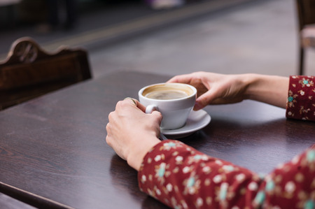 The hands of a young woman with a cup of coffee on a table outside in the streetの写真素材