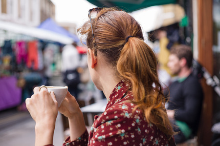 A young woman is having a cup of coffee outside at a table on the streetの写真素材