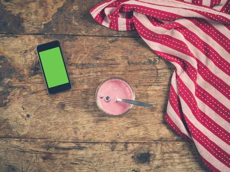 Overhead shot of yogurt and smart phone with a green screen on a wooden table with a tea towelの写真素材