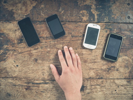 Overhead shot of a male hand resting on a wooden table with a selection of smart phonesの写真素材