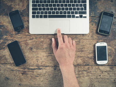Overhead shot of a male hand using a laptop computer surrounded by a selection of smart phonesの写真素材