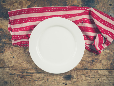 Overhead shot of a white plate and a tea towel on a wooden tableの写真素材