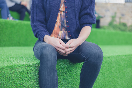 A young woman is sitting outside on some steps covered in astro turfの写真素材
