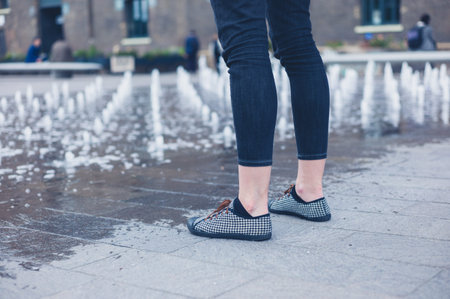 The legs of a young woman as she is standing by a small fountain in the city