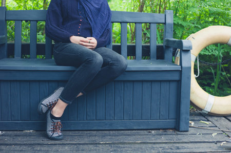 A young woman is sitting on a bench outside in natureの写真素材