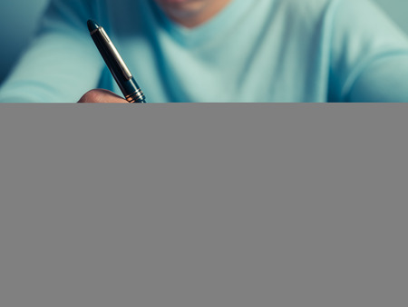 A young man is sitting at a table and is writing in a notebookの写真素材