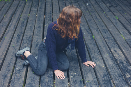 A young woman is sitting on a big wooden deckの写真素材