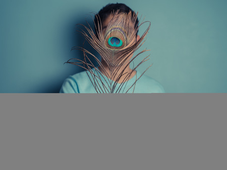 A young man is holding a pretty peacock featherの写真素材