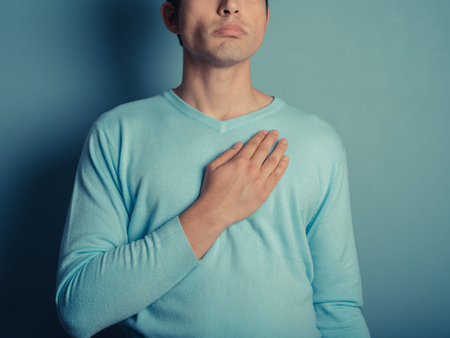 A young man wearing a blue jumper is placing his hand on his chest