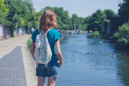 A young woman is standing by a canal in the city on a summer dayの写真素材