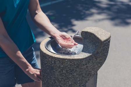A young woman is standing by a water fountain in the park on a summer dayの写真素材