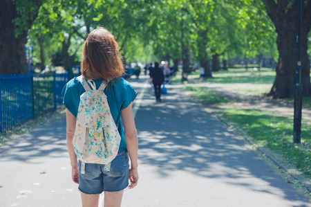 A young woman wearing a bacpack is standig on a path in the park on a summer dayの写真素材