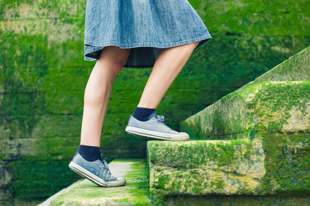 A young woman wearing a skirt is walking up some stairs by the sea covered in green mossの写真素材