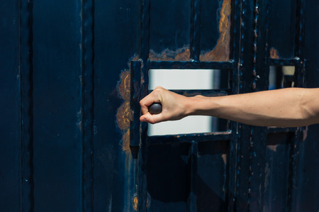 A young female hand is grapping the hand handle of a gate and is opening itの写真素材