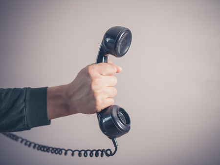 The hand of a young man is holding a vintage rotary telephoneの写真素材