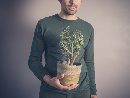 A young man wearing a green top is holding a potted plantの写真素材