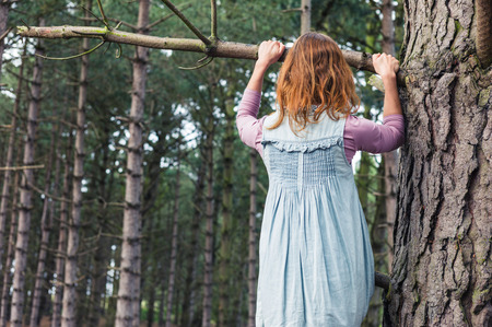 A young woman is climbing a tree in the forestの写真素材