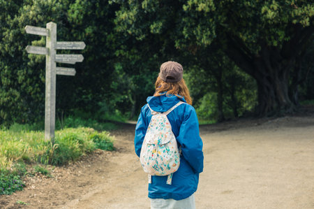 A young woman is trekking and is looking at a signpost in the forest