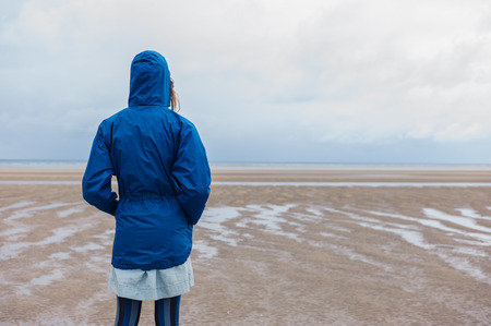 A young woman wearing a blue waterproof jacket is walking on the beach on a cold dayの写真素材
