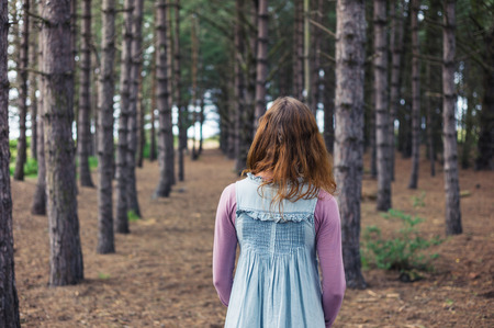 A young woman is standing in a clearing in the forest and is looking at the treesの写真素材