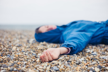 An unconscious woman is lying on a shingle beachの写真素材
