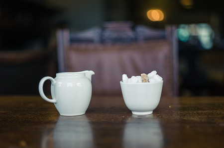 A pot of milk and a bowl of sugar cubes on a dinner table in a dining roomの写真素材