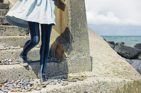 The legs of a young woman wearing a dress as she is standing on some stairs by the coastの写真素材