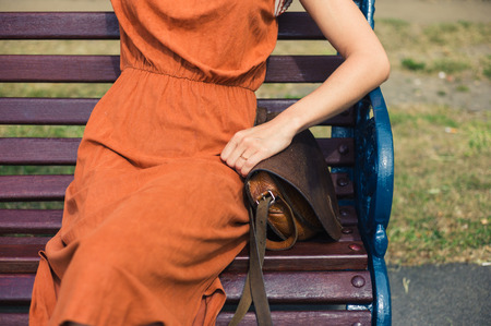 A young woman is sitting on a park bench on a sunny day in the summerの写真素材