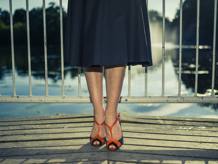 Vintage filtered shot of the legs and feet of an elegant woman standing on a pier by a lake in a parkの写真素材