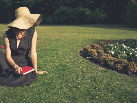 Vintage filtered shot of an elegant woman sitting on the grass in a park with a bookの写真素材