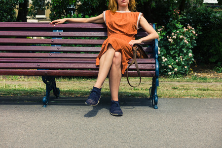 A young woman is sitting on a park bench on a sunny day in the summerの写真素材