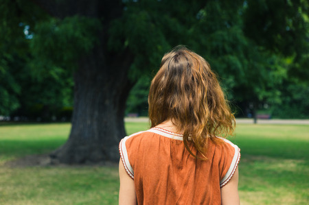 A young woman is walking in a park and is standing by a big treeの写真素材