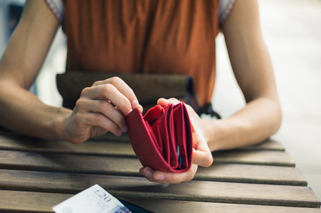 A young woman is sitting outside and is opening her purse to get some cash for paying her bill at a cafeの写真素材