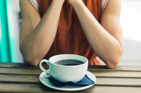 A young woman is sitting at a table outside and is having a big cup of coffeeの写真素材