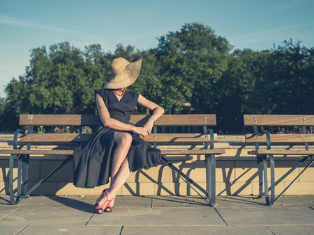 Vintage filtered shot of an elegant young woman in dress and high heels sitting on a park benchの写真素材