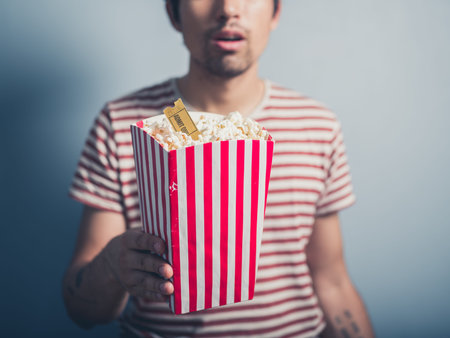 A young man is holding a box of popcorn with a cinema ticket in it