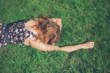 A young woman wearing a dress is lying in the green grass on a sunny summer dayの写真素材