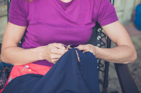 A young woman is sitting outside and is sewing a piece of clothingの写真素材