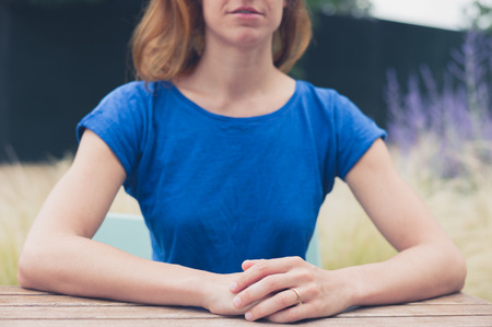 A young woman is sitting at a table outside in summerの写真素材
