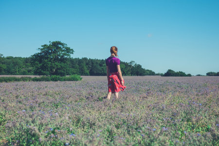 A young woman is standing in a field of purple flowers on a sunny summer dayの写真素材