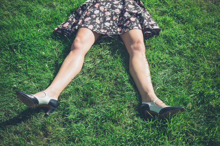 The legs of a young woman wearing a dress as she is lying on the grass in a fieldの写真素材