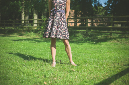 A young woman wearing a dress is standing in a field near a fence on a summer dayの写真素材