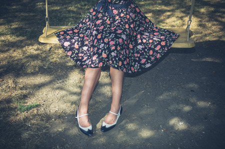 A young woman wearing a dress is sitting on a swing outside on a summer dayの写真素材