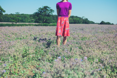 A young woman is standing in a field of purple flowers on a sunny summer dayの写真素材