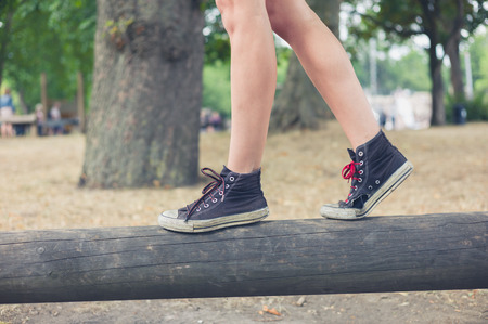 The feet of a young woman as she is walking on a wooden beam outside in the parkの写真素材